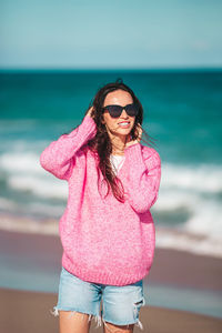 Young woman wearing sunglasses standing at beach against sky