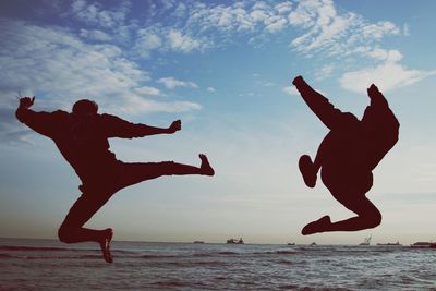 Silhouette friends jumping at beach against sky