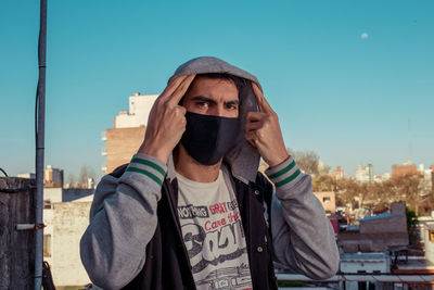 Portrait of young man with face mask in city against clear sky