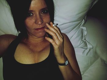 Portrait of woman holding cigarette while relaxing on bed at home