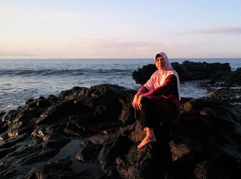 Woman sitting on rock by sea against sky