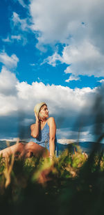 Woman siting by in grassland against sky