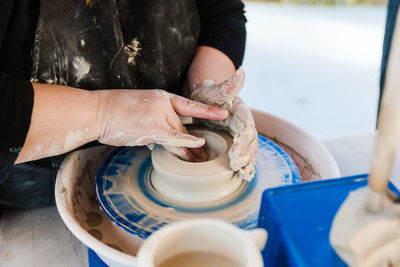 Crop anonymous female artisan in apron modeling clay pot on throwing wheel