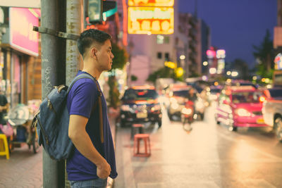 Side view of young man looking at city street at night