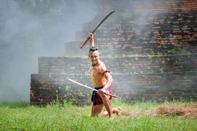 Full length portrait of shirtless warrior with swords on grassy field