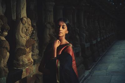 Young woman wearing sari while standing by statues in temple