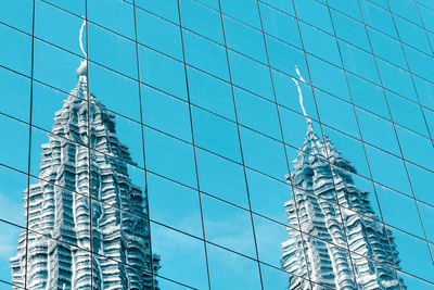 Reflection of twin towers on the glass building against blue sky