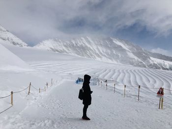 Side view of woman standing on snow covered land against sky