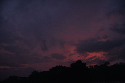 Low angle view of silhouette trees against dramatic sky