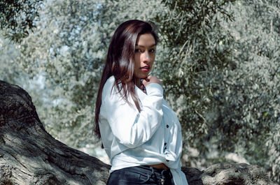 Portrait of young woman standing against tree trunk