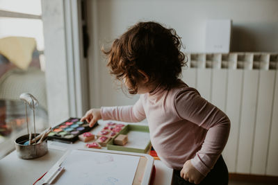 Midsection of child painting with watercolor at home