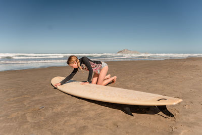 Young female waxing surfboard at a beach in new zealand