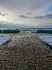 Footpath by sea against sky during sunset