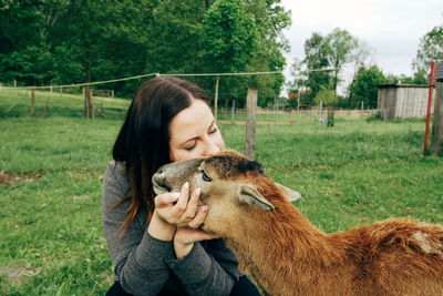 Young woman with goat on grassy field