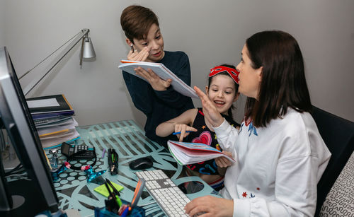 Daughter and son holding books by mother using computer on table