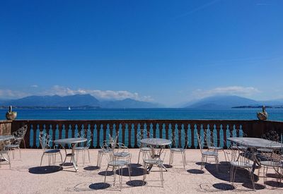 Tables and chairs arrangement on terrace at restaurant by sea against blue sky