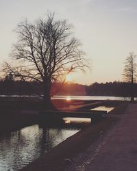Silhouette bare trees by lake against sky during sunset