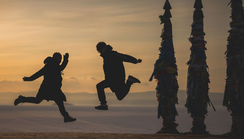 Full length of mature man jumping with son against sky during sunset