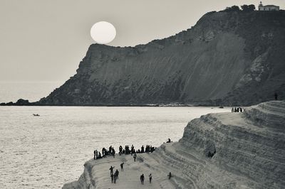 Group of people on rock by sea against sky