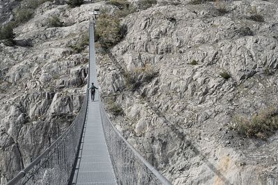 Rear view of man walking amidst rock formations on footbridge