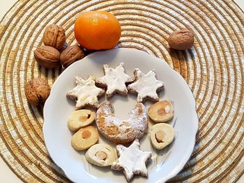 Still life of cookies on porcelain plate, mandarin-orange and walnuts beside on place mat