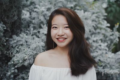 Portrait of smiling young woman by plants at public park