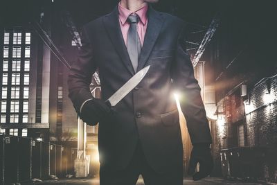 Midsection of man wearing suit holding knife at night