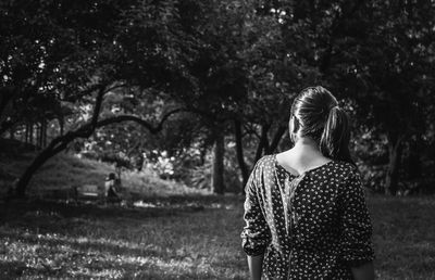 Rear view of mid adult woman standing against trees