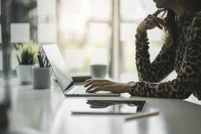 Midsection of woman using mobile phone while sitting on table