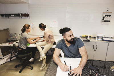 Male engineer smiling on table with colleagues working in background