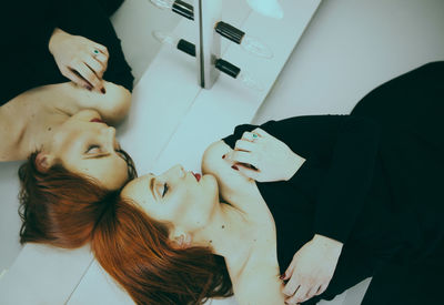 High angle view of young woman resting on table with reflection on mirror