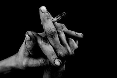 Close-up of cropped dirty hands holding cigarette against black background