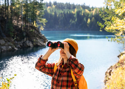 Side view of woman photographing while standing against lake