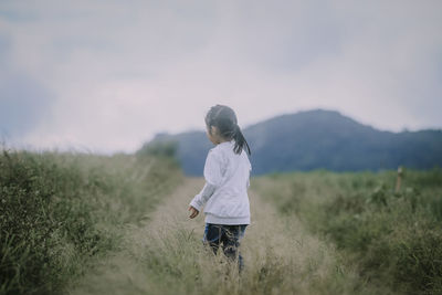 Rear view of woman walking on field against sky