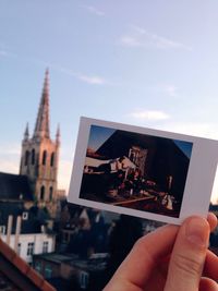 Cropped image of person holding instant print transfer against sky