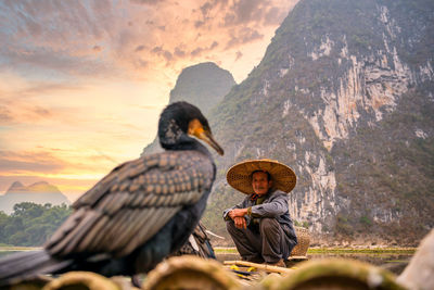 Man sitting on mountain against sky during sunset