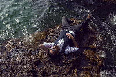 Man with a beard in dark clothes and white shirt lie on the stone seashore in the crimea tarkhankut