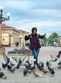 Woman teenager feeding pigeons with seeds on wide pedestrian city street, urban bird catches food