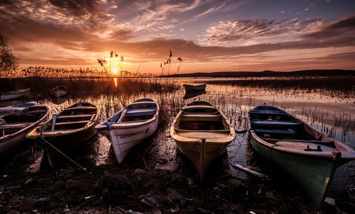 Boats moored on shore against sky during sunset