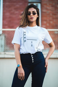 Portrait of young woman wearing sunglasses standing against brick wall