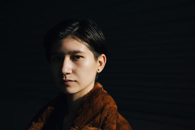 Portrait of female wearing nose ring against black background