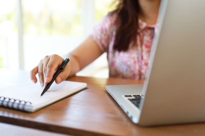 Midsection of woman using mobile phone while sitting on table