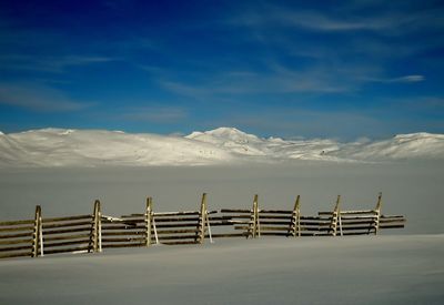 Deck chairs on snow covered landscape against sky