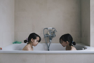 Twin sister bathing together in bathtub at home