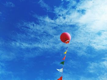 Low angle view of helium balloon with bunting in mid-air against blue sky