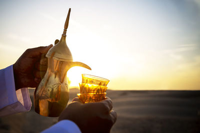 Person holding ice cream at beach against sky during sunset