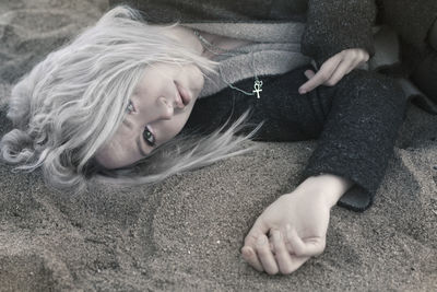 High angle portrait of sad woman lying on sand at beach