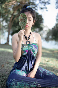 Young woman holding leaf while sitting on field