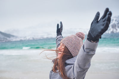 Smiling woman with arms raised standing outdoors during winter
