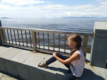 Side view of woman sitting by railing against sea
